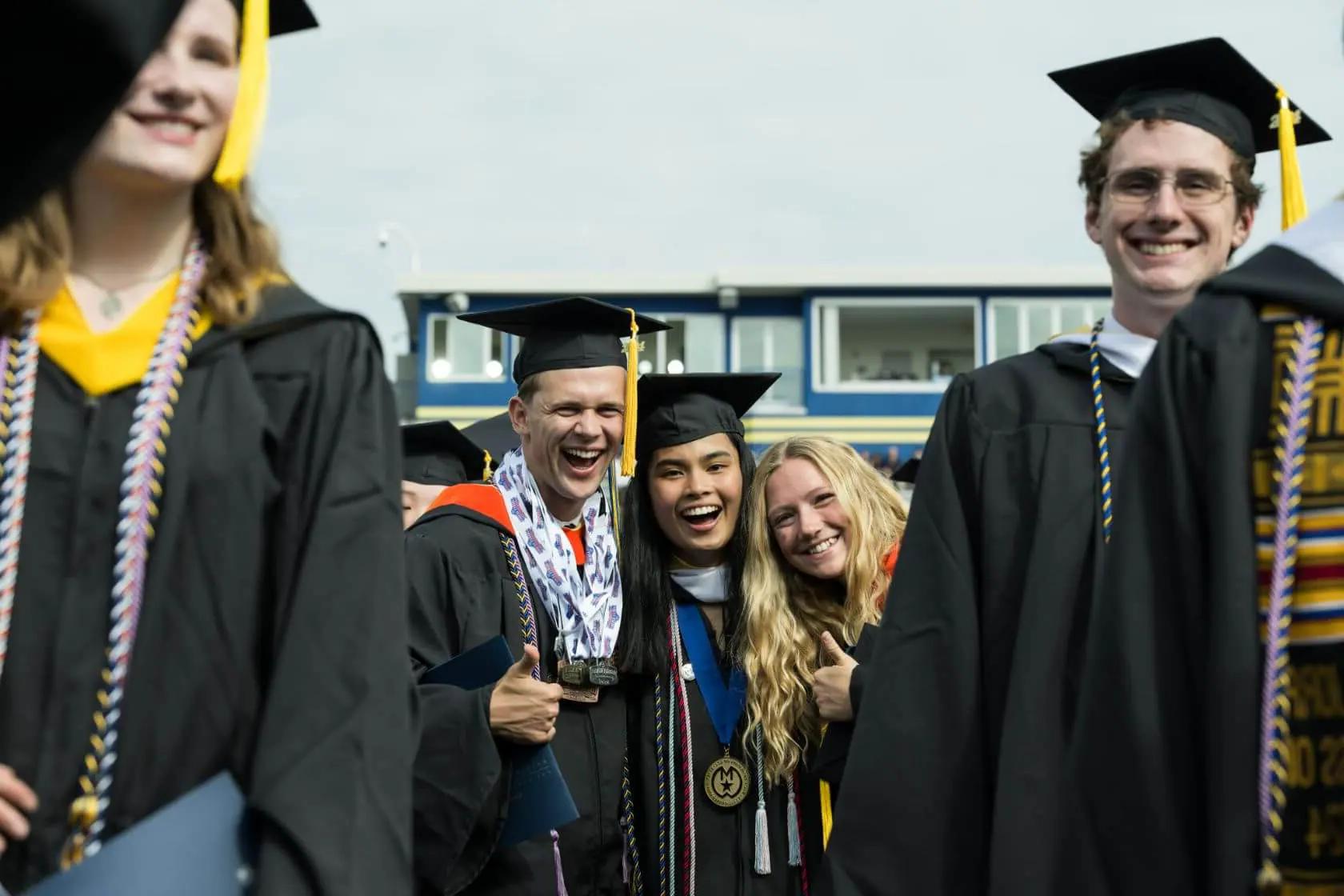 一群头戴帽子、身穿长袍的毕业生对着镜头微笑.